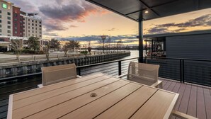 Uma área de estar coberta ao ar livre com vista para a orla e um hotel ao fundo.