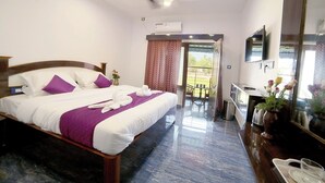 A hotel room with a bed, a desk, a TV, and a balcony with a view. - Hotel Sea Tides (Mahabalipuram)