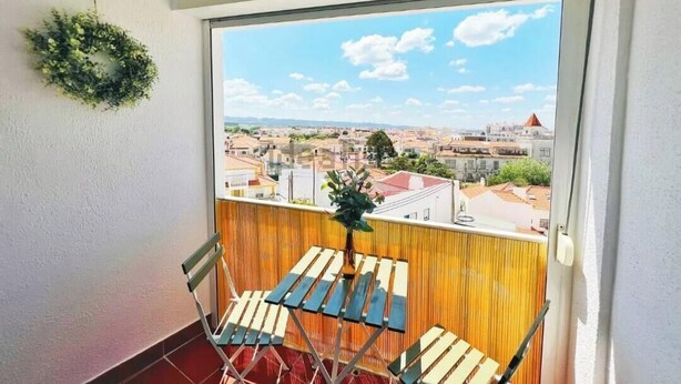 Ein Balkon mit Blick auf eine Stadtansicht, einem Holztisch und einem Stuhl.