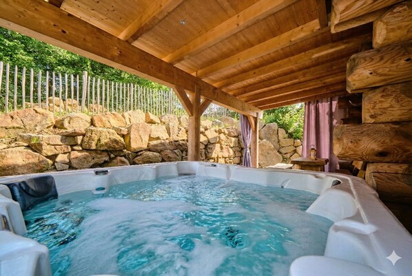 Ein Whirlpool unter einer Holzhütte mit einer Steinwand und einem Zaun im Hintergrund.