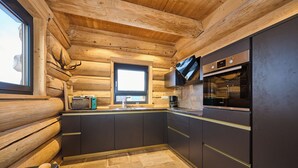 A modern kitchen with dark cabinets, a built-in oven, and a window above the sink. - Log cabin chalet WoidSinn (Spiegelau)