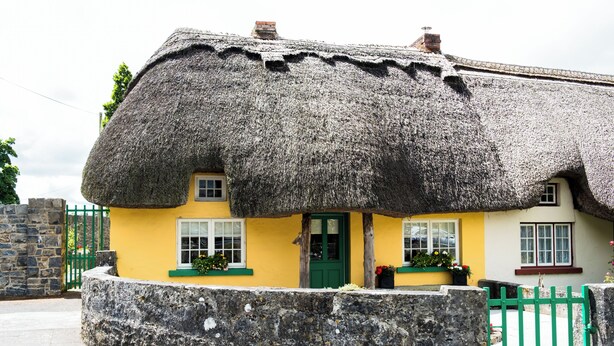 A traditional thatched-roof house with a stone wall in front, a green door, and windows with white frames. - Beautiful 200 year old thatched cottage in the picturesque village of Adare (Adare)