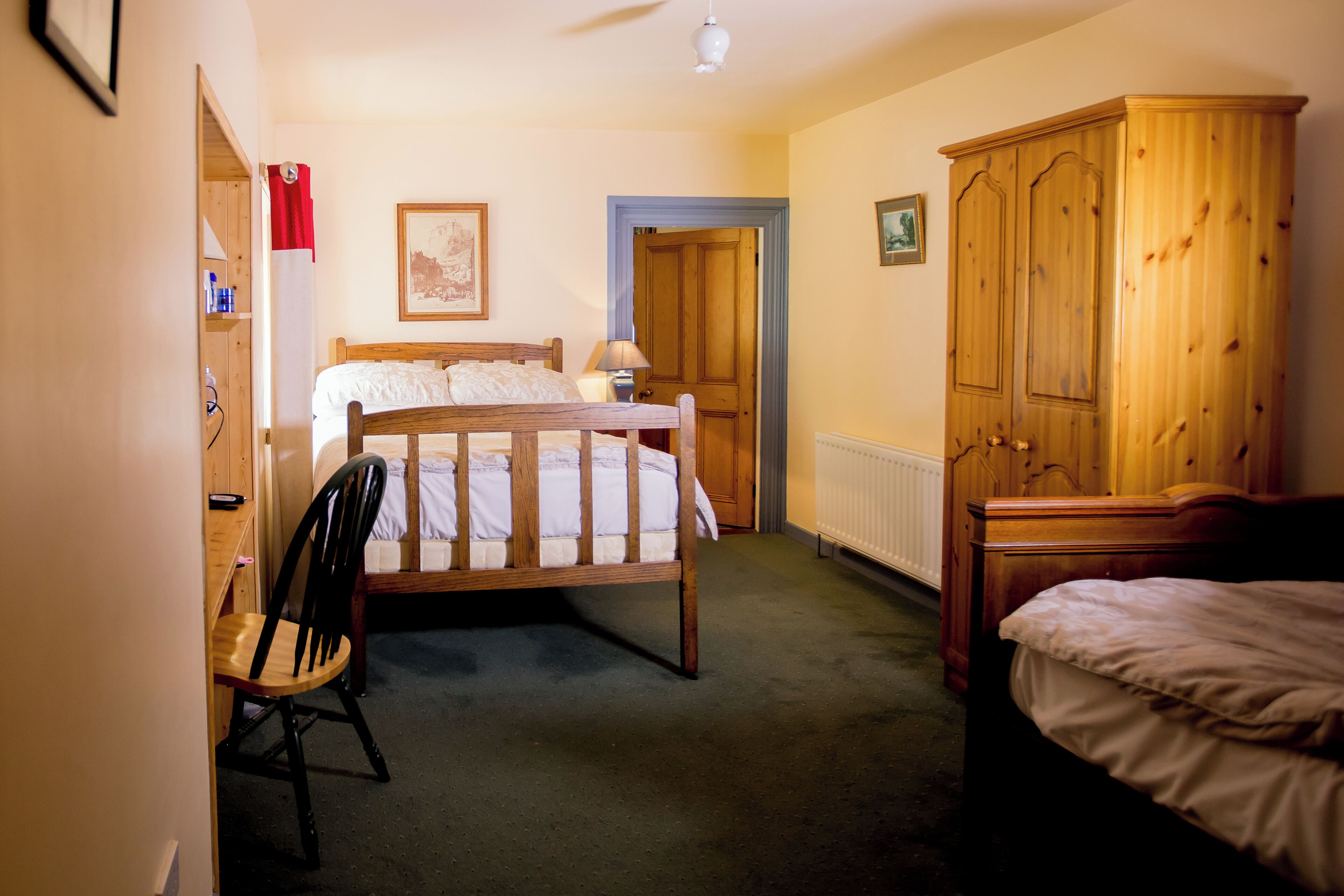Quarto com cama de madeira, guarda-roupa de madeira, cadeira e escrivaninha com abajur.