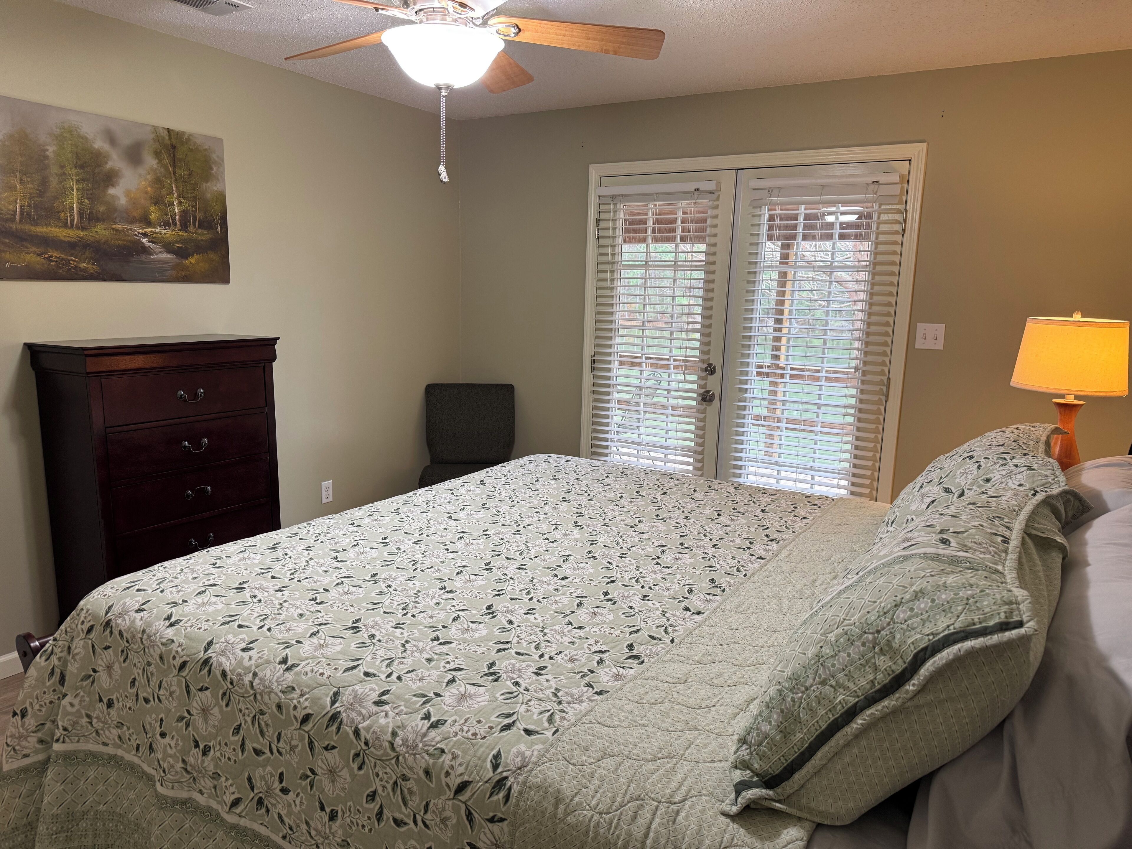 A bedroom with a bed, a dresser, a ceiling fan, and a window with blinds.