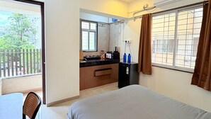 A bedroom with a bed, a ceiling fan, a window with curtains, a kitchenette, and a balcony. - Wren Hideaway:Cozy AC Studio in Pune (Pimpri-Chinchwad)