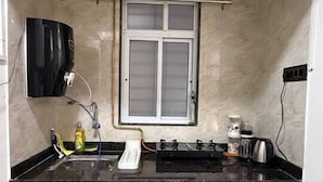 A compact kitchen with a black countertop, a window, a built-in stove, and a sink. - Falcon: Cozy AC Studio Flat by Bleisure Hosting (Pimpri-Chinchwad)