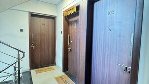 A hotel corridor with wooden doors numbered 101 and 103, a metal staircase, and welcome mats on the floor. - Falcon: Cozy AC Studio Flat by Bleisure Hosting (Pimpri-Chinchwad)