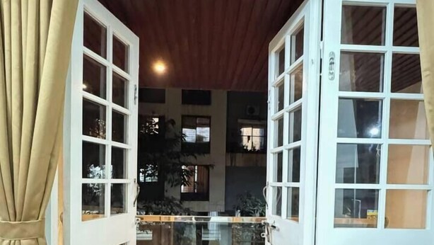 Blick durch geöffnete französische Türen zu einem überdachten Außenbereich mit Holzboden und Glasgeländern.