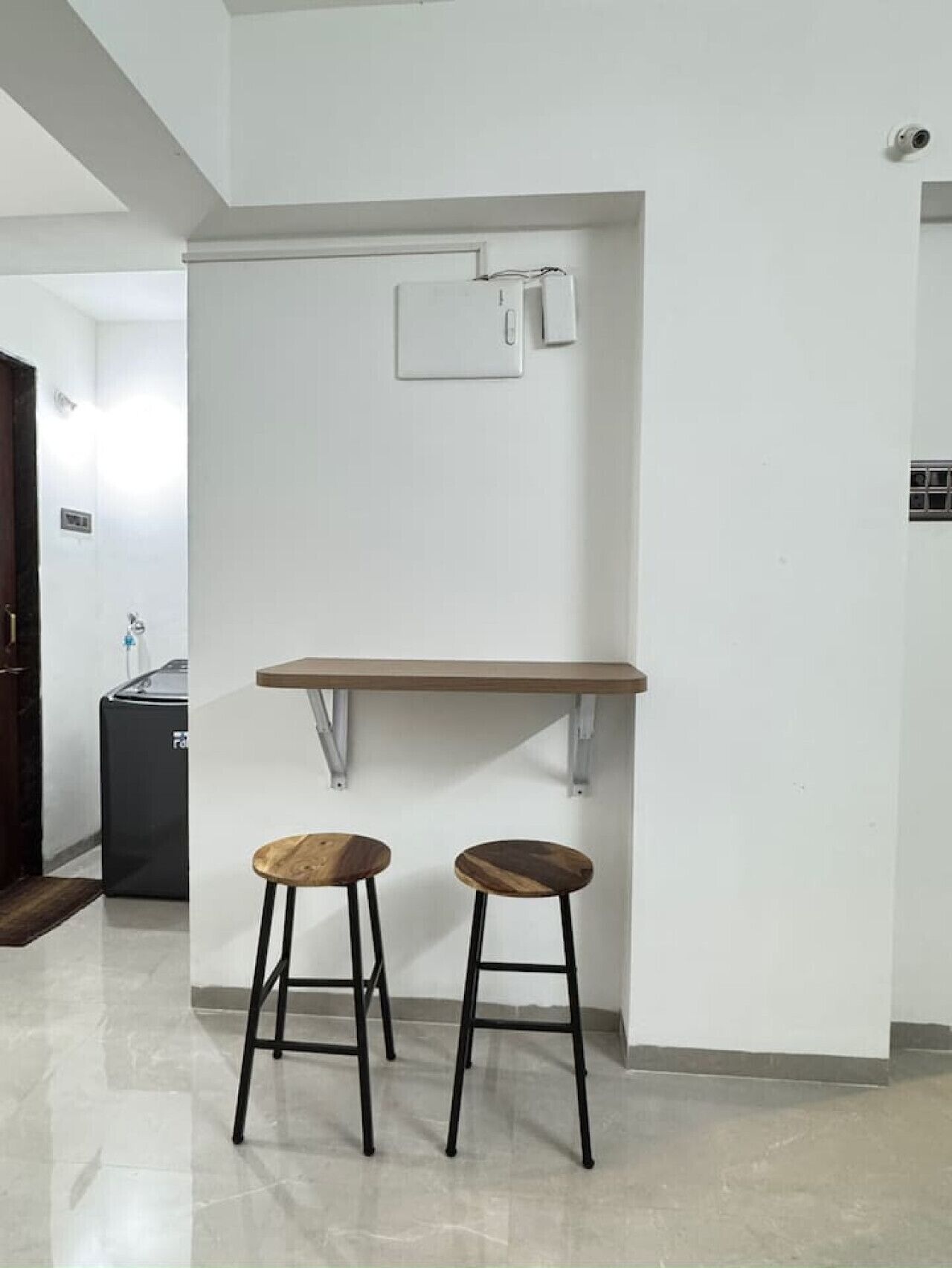 Een compact, modern kitchenette met een wit aanrecht, twee krukken en een wandplank.