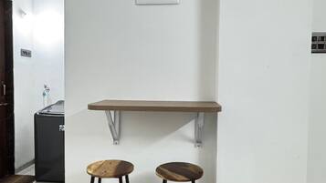 Een compact, modern kitchenette met een wit aanrecht, twee krukken en een wandplank.