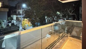 Ein Balkon mit Holzboden und Glasgeländer, der auf eine belebte Straße bei Nacht blickt.