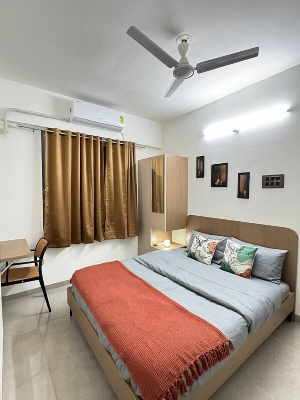 A bedroom with a bed, a desk, a chair, a ceiling fan, and a window with curtains.