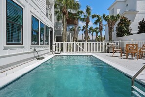 A swimming pool with a white fence, palm trees, and outdoor furniture. - Beach Music Gorgeous 6 Bdrm, steps to beach, 6 seater golf cart (Santa Rosa Beach)