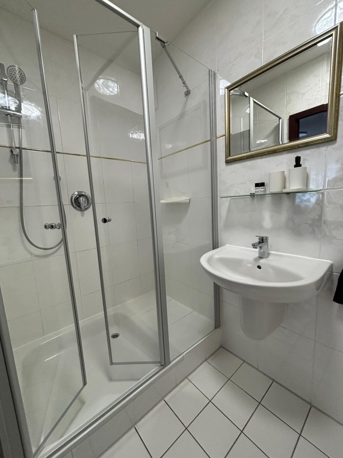 A bathroom with a glass-enclosed shower, a white sink, and a mirror with a gold frame.
