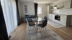 A modern kitchen with white cabinets, a dining area with a round table and chairs, and a living area with a sofa and artwork on the wall. - Turmhotel Scharbeutz (Scharbeutz)