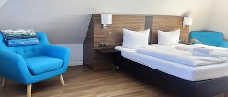 Una habitación de hotel con una cama, un sillón azul, una mesita de noche y una lámpara de pared.