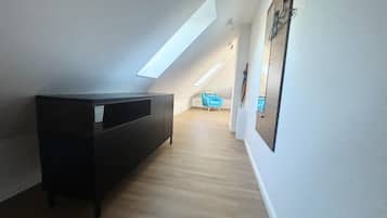 Un pasillo estrecho con un mueble oscuro, una silla azul y un techo inclinado con tragaluces.