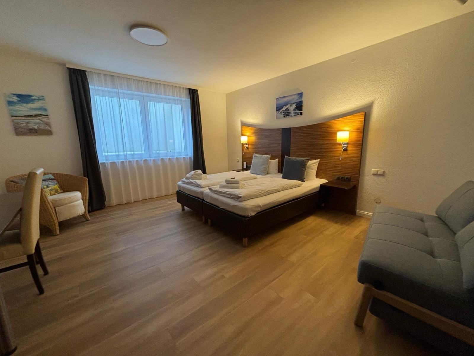 Ein Hotelzimmer mit einem Doppelbett, einem kleinen Sessel, einer Couch, einem Fenster mit Vorhängen und einem Bild an der Wand.