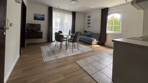 A modern living room with a sofa, a dining table with chairs, a TV, and a window with curtains. - Turmhotel Scharbeutz (Scharbeutz)