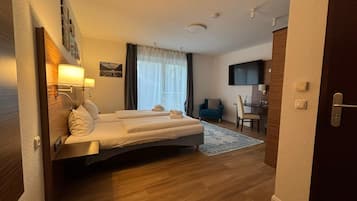 Een hotelkamer met een bed, bureau, stoel, televisie en raam met gordijnen.