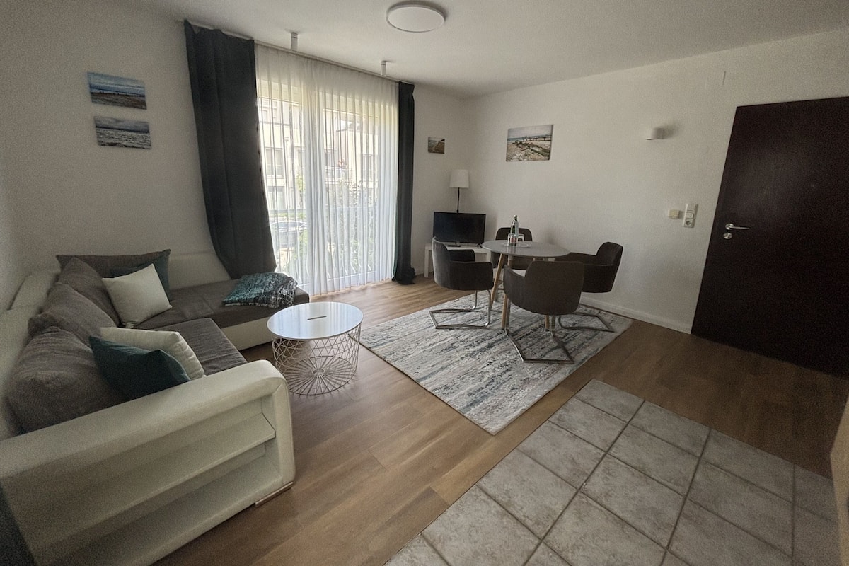 A living room with a sofa, a coffee table, a dining table with chairs, a TV, and a door.