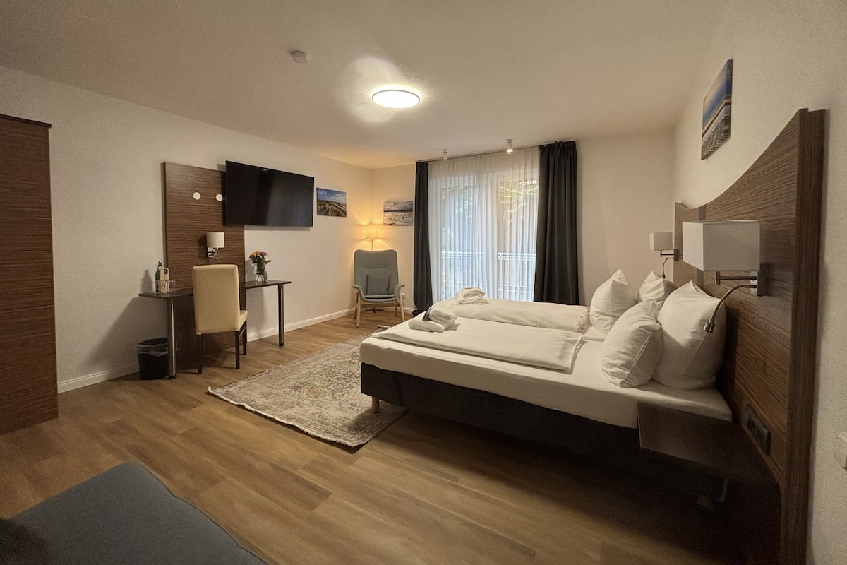 A hotel room with a bed, a desk, a chair, a TV, and a window with curtains.