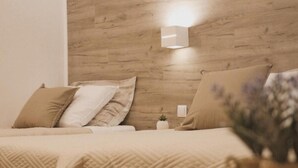 A bedroom with a wooden headboard, a bed with beige bedding, and a small bedside table with a lamp. - Hotel Orion Vodice - Triple bedroom 2 (Vodice)