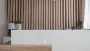 A reception desk with a wooden slat wall, a white counter, and a small potted plant. - Hotel Orion Vodice - Triple bedroom 4 (Vodice)