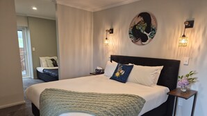 Un dormitorio moderno con una cama grande, cabecera, dos lámparas de noche, un elemento decorativo en la pared y una mesita con un florero.