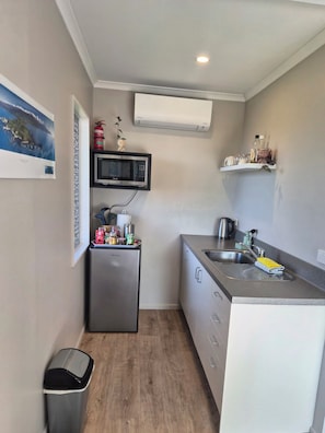 A compact kitchen with a refrigerator, microwave, sink, and a small trash bin. - Centrally located Hilltop Apartment (Kaikōura)