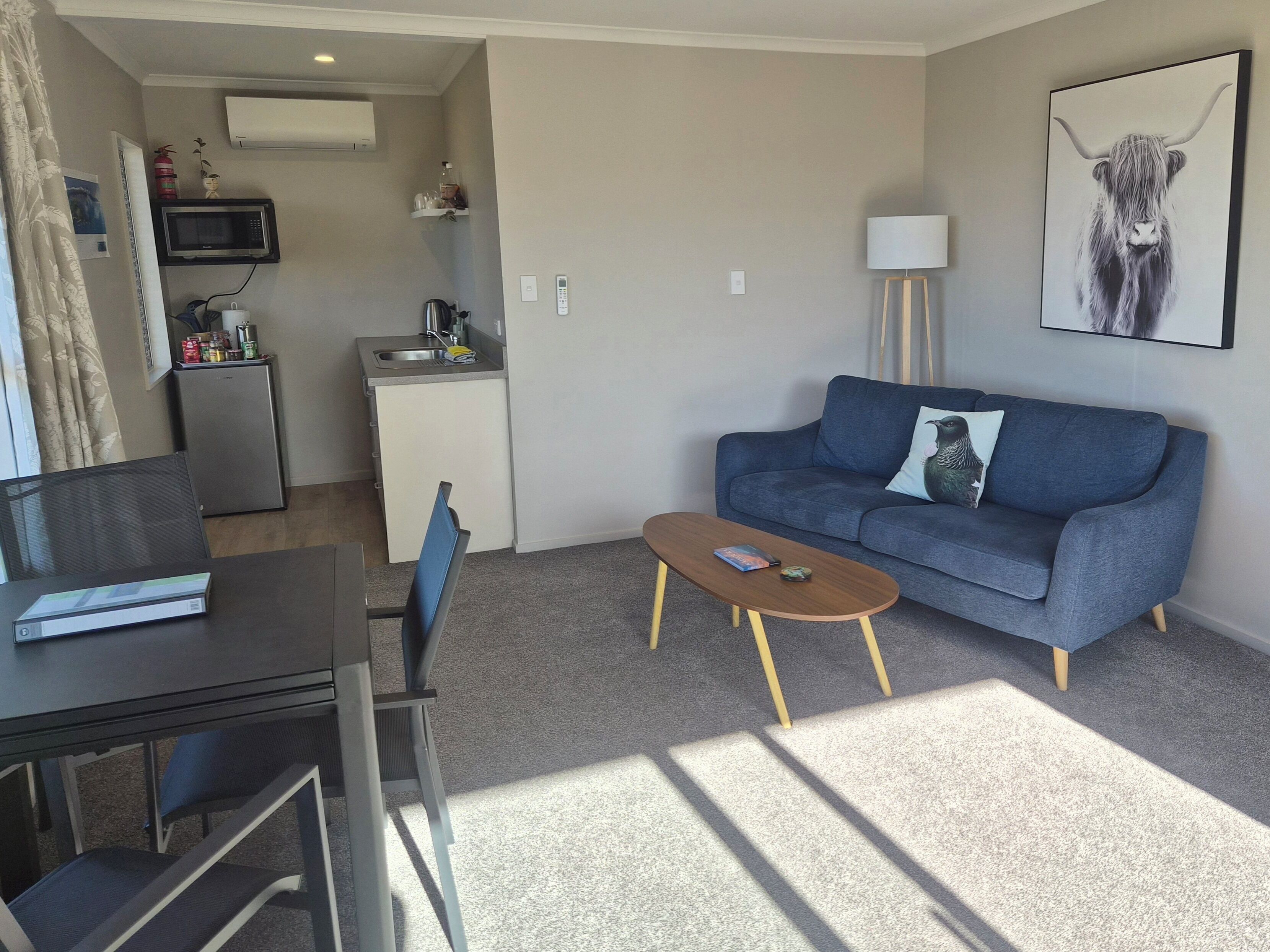 A living room with a sofa, coffee table, TV, kitchenette, and a painting on the wall.