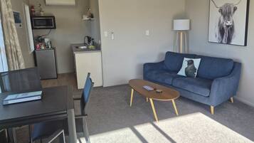 A living room with a sofa, coffee table, TV, kitchenette, and a painting on the wall.