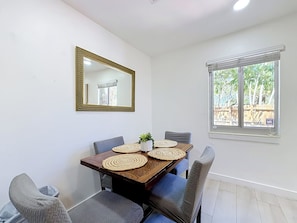 Un espace repas comprenant une table, des chaises, un miroir et une fenêtre donnant sur un paysage verdoyant.