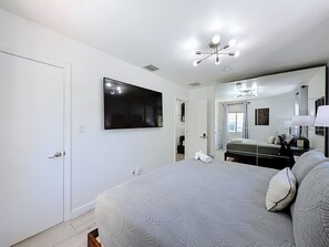 A bedroom with a bed, a TV, a mirror, a ceiling light fixture, and a door. - Pool House in Fort Lauderdale (Fort Lauderdale)