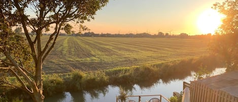 Une vue sur la rivière, avec une terrasse en bois, des chaises et un petit bateau.
