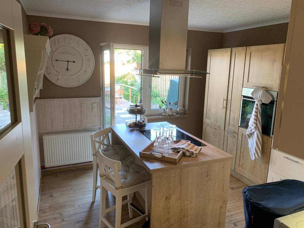 Eine Küche mit einer Holzinsel, einer Wanduhr und einem Fenster mit Blick auf einen Garten.