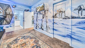 A hallway with a large mural of a snowy landscape and a robot. There is a patterned rug on the floor and a door with a mirror. - Comfortable 4 bedroom 4 bath Home Near Disney (Davenport)