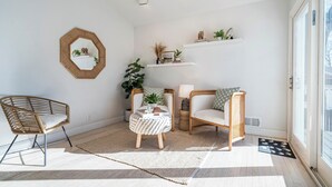 Een lichte kamer met een groot raam, een ronde spiegel en twee rieten stoelen.