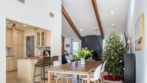 Een moderne keuken met houten kasten, een eethoek met een houten tafel en stoelen, en een kerstboom.