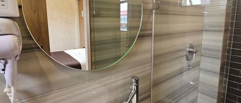 Un baño moderno con un espejo ovalado grande, un lavamanos redondo y un secador de pelo de mano.