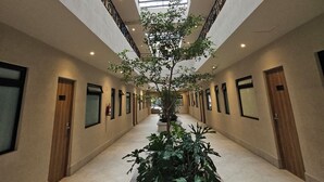 A hotel corridor with a central planter, glass ceiling, and doors on either side. - Hotel Único La Villa (Mexico City)