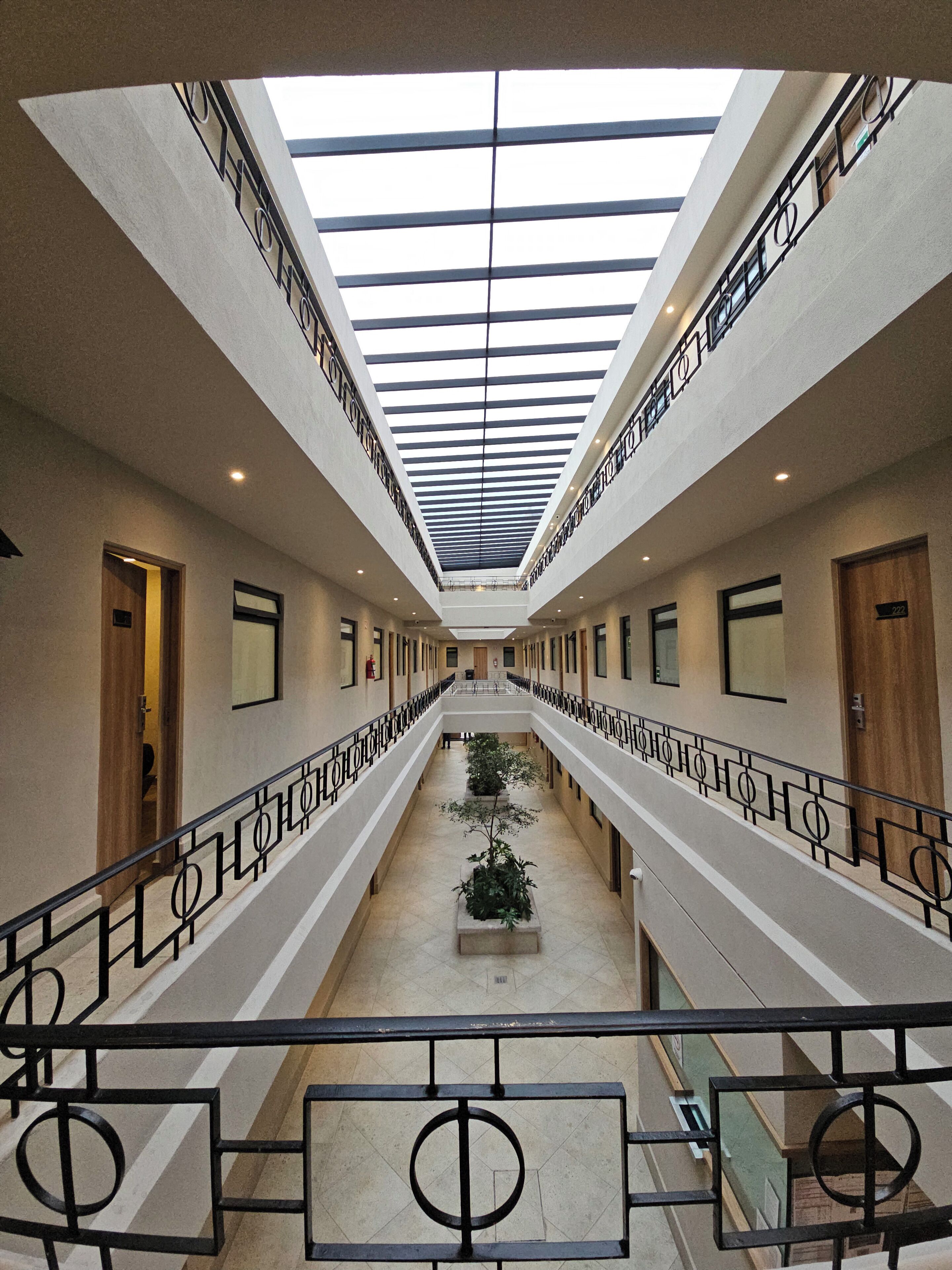 Un pasillo de hotel con un atrio central, balcones dobles y un tragaluz.
