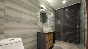 A modern bathroom with a marble wall, a white toilet, a wooden vanity with a sink, and a glass shower enclosure. - Hotel Único La Villa (Mexico City)