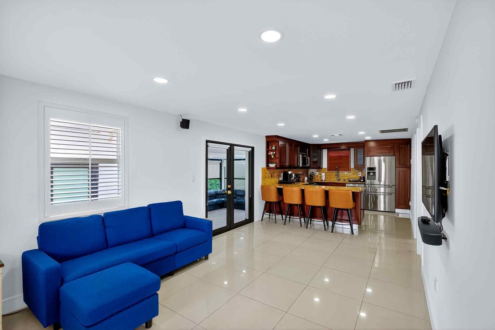 A modern living room with a blue sofa, a kitchen area with a dining set, and a TV mounted on the wall.