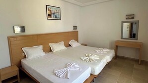 Ein Hotelzimmer mit zwei Betten, einem hölzernen Kopfteil, einem kleinen Nachttisch, einem Beistelltisch, einem gerahmten Bild an der Wand und einem Spiegel auf einer Holzkonsole.