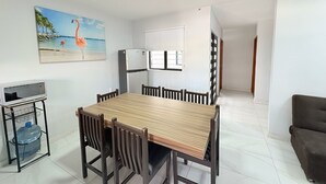 Ein Essbereich mit Holztisch und Stühlen, einem Kühlschrank, einer Mikrowelle auf einem Wagen und einem Bild einer Strandlandschaft.