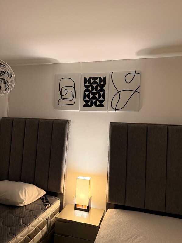A bedroom with two beds, a bedside table with a lamp, and three wall art pieces.
