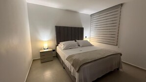 A bedroom with a bed, a nightstand, a lamp, and a window with blinds. - Suite 1103 (ideal for family travel) (San Gil)
