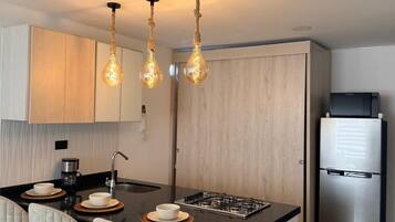 A modern kitchen with a central island, bar stools, a stainless steel refrigerator, and pendant lighting.