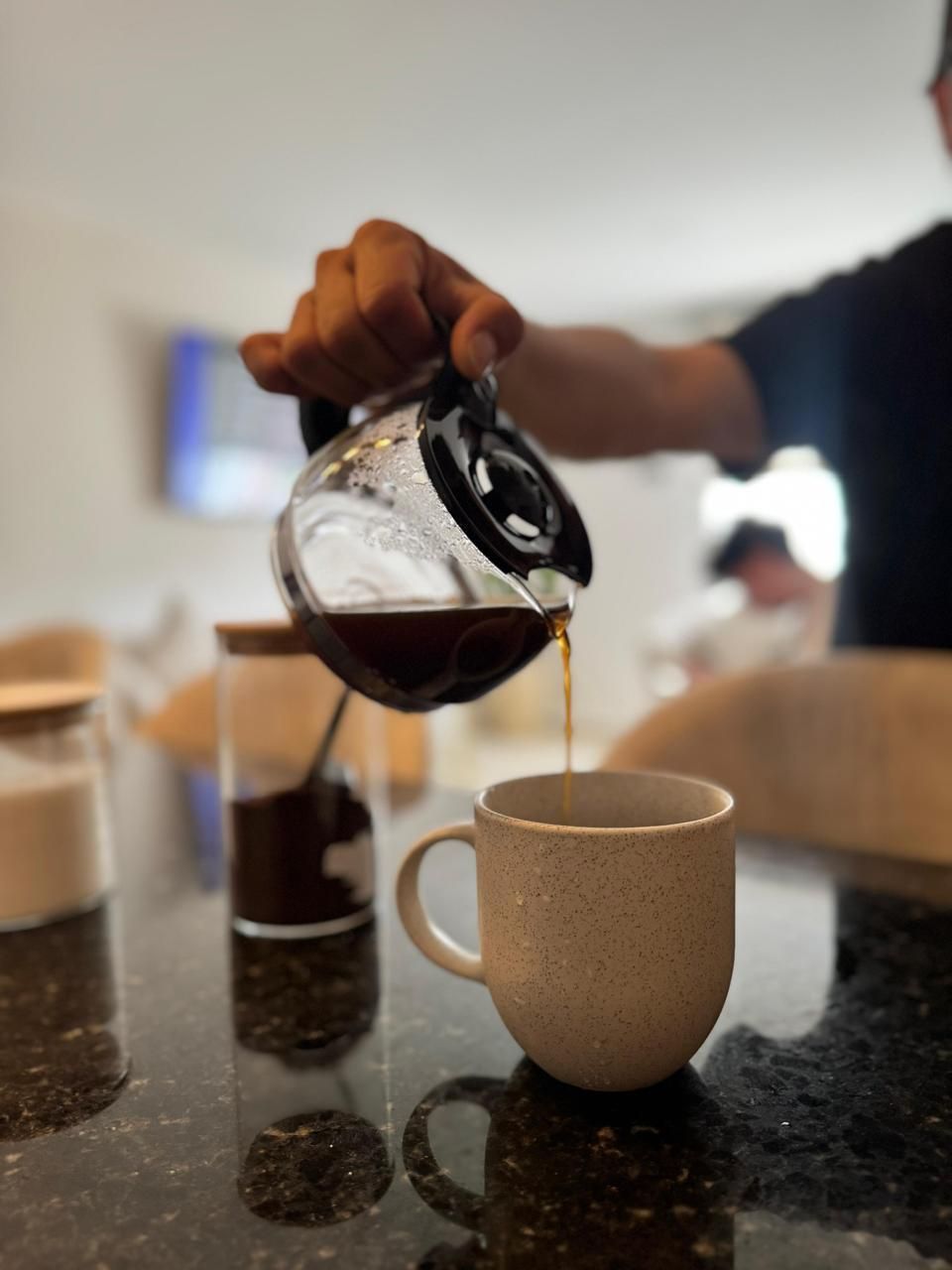 A hand pouring coffee into a mug on a kitchen counter.